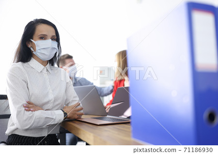 Employees in protective medical masks are sitting in office at their desk. 71186930