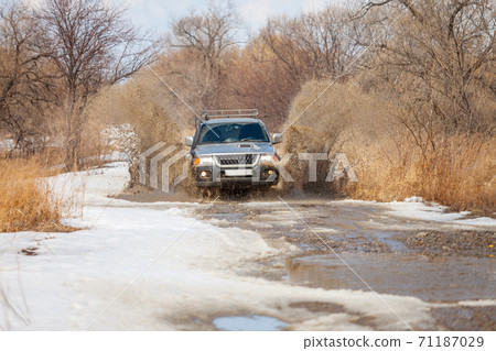 Mitsubishi Pajero Sport on dirt road in early spring making splashes from a puddle 71187029