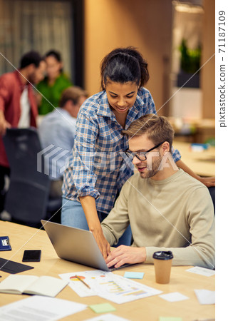 Mentoring in office. Two young multiracial colleagues using laptop and discussing project, mixed race woman helping male coworker with computer work Mentoring in office. Two young multiracial colleagues using laptop and discussing project, mixed race woman helping male coworker with computer work 71187109