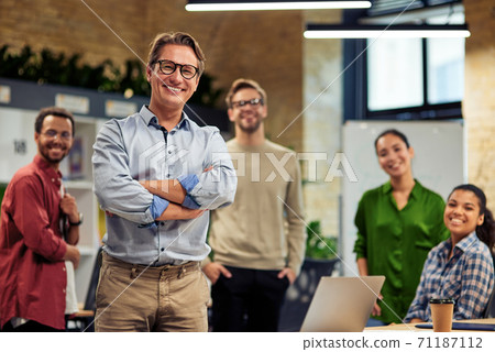 Happy startup team. Group of cheerful multiracial business people smiling at camera while standing in the modern office, working together Happy startup team. Group of cheerful multiracial business people smiling at camera while standing in the modern office, working together 71187112