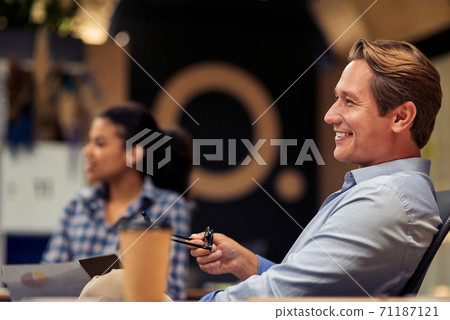 Happy cheerful mature businessman holding eyeglasses and smiling while working with colleagues in the modern office Happy cheerful mature businessman holding eyeglasses and smiling while working with colleagues in the modern office 71187121
