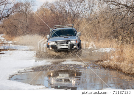 SUV on dirt road in early spring making splashes from a puddle SUV on dirt road in early spring making splashes from a puddle 71187123