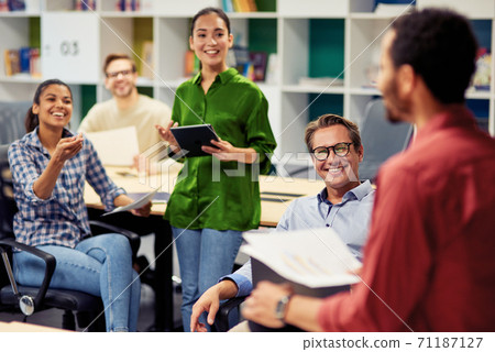 Positive team. Group of young happy multi racial business people communicating and sharing ideas while working together in the modern office Positive team. Group of young happy multi racial business people communicating and sharing ideas while working together in the modern office 71187127