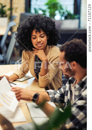 Two young diverse coworkers analyzing sales report while working together in the office Two young diverse coworkers analyzing sales report while working together in the office 71187129