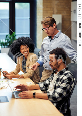 Three multiracial colleagues working together in the modern office, looking at laptop screen and discussing something Three multiracial colleagues working together in the modern office, looking at laptop screen and discussing something 71187131