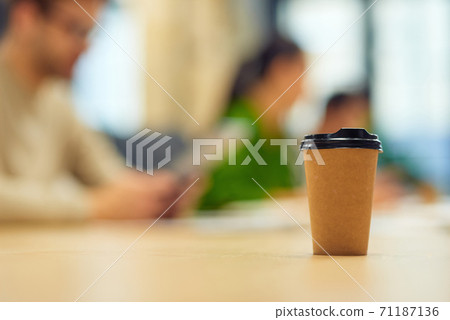 Paper coffee cup standing on the table in office with people working on the background 71187136