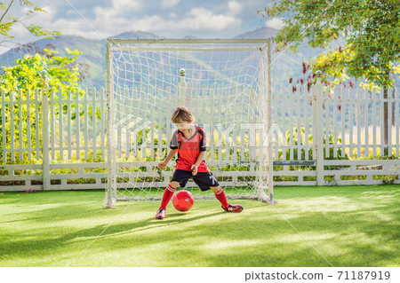 Little cute kid boy in red football uniform playing soccer, football on field, outdoors. Active child making sports with kids or father, Smiling happy boy having fun in summer Little cute kid boy in red football uniform playing soccer, football on field, outdoors. Active child making sports with kids or father, Smiling happy boy having fun in summer 71187919