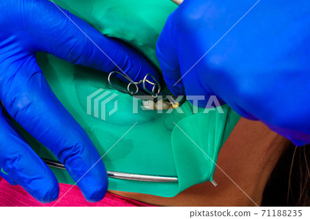 The dentist treats the patient's tooth with a rubber dam, drill, mirror. The dentist treats the patient's tooth with a rubber dam, drill, mirror. 71188235