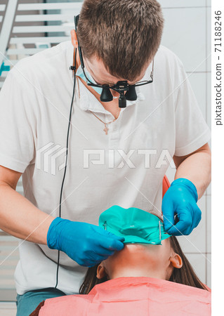 Installation of a rubber dam with a metal clamp for dental fillings, sterile and modern dental treatment. Installation of a rubber dam with a metal clamp for dental fillings, sterile and modern dental treatment. 71188246