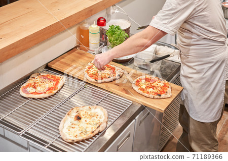Italian kitchen and cooking concept. Chief with a pizza cutter cutting pizza to pieces at Neapolitan pizzeria. 71189366