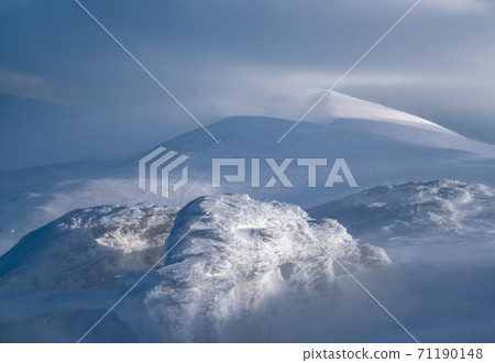Snow covered winter mountains  in last evening sunlight. Magnificent windy dusk on tops above picturesque alpine ski resort 71190148