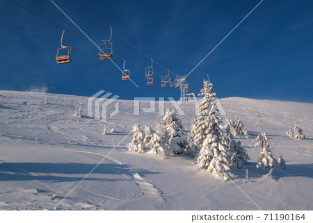 Alpine resort ski lift with seats going over the sunrise mountain skiing freeride slopes and fir tree groves Alpine resort ski lift with seats going over the sunrise mountain skiing freeride slopes and fir tree groves 71190164