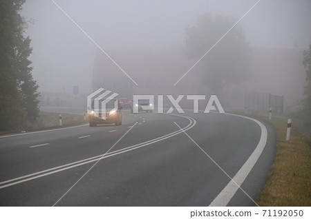 Car on the road in the fog. Autumn landscape - dangerous road traffic in winter season. 71192050