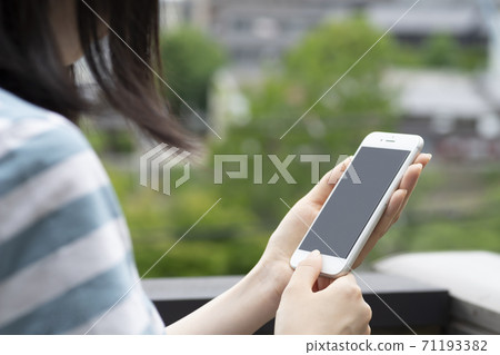 A woman operating a smartphone on the balcony A woman operating a smartphone on the balcony 71193382