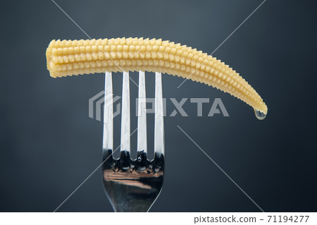 pickled corn on a fork close-up on a dark background. food and vegetables 71194277