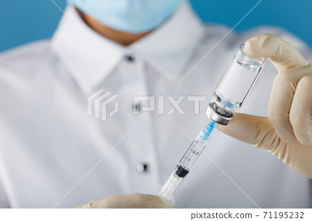 A doctor in rubber gloves holds an ampoule with a vaccine and a syringe, close-up. A doctor in rubber gloves holds an ampoule with a vaccine and a syringe, close-up. 71195232