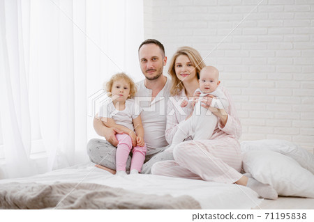 A young Caucasian family with two children daughters in a white home interior. Home clothes. 71195838