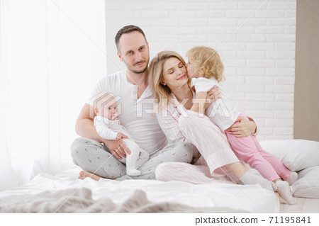 A young Caucasian family with two children daughters in a white home interior. Home clothes. 71195841