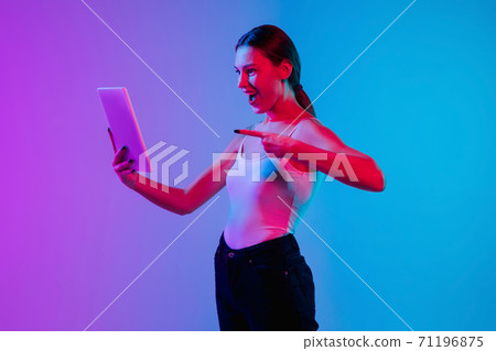 Young caucasian woman's portrait on gradient blue-purple studio background in neon light 71196875