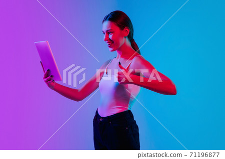 Young caucasian woman's portrait on gradient blue-purple studio background in neon light Young caucasian woman's portrait on gradient blue-purple studio background in neon light 71196877