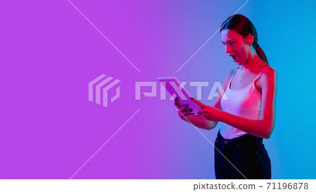 Young caucasian woman's portrait on gradient blue-purple studio background in neon light 71196878