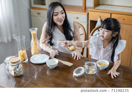 Mother sit looking at the daughter playing in the kitchen. Mother sit looking at the daughter playing in the kitchen. 71198235