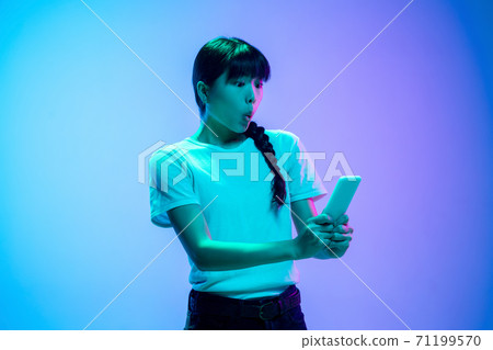 Young asian woman's portrait on gradient blue-purple studio background in neon light Young asian woman's portrait on gradient blue-purple studio background in neon light 71199570