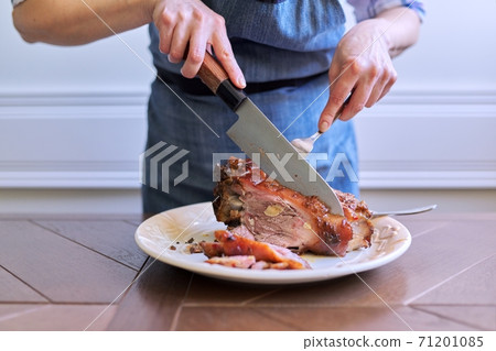 Female hands cutting freshly cooked hot meat on plate 71201085