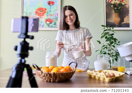 Girl teenager food blogger cooking orange pancakes at home in kitchen, smiling to the camera 71201143