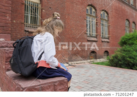 Girl child with backpack sitting in school yard reading notebook, copy space Girl child with backpack sitting in school yard reading notebook, copy space 71201247