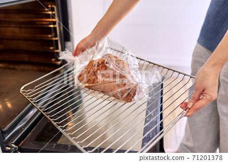 Hands woman cooking pork at home in baking sleeve, puts tray of meat in oven Hands woman cooking pork at home in baking sleeve, puts tray of meat in oven 71201378