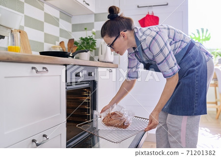 Woman preparing pork in baking sleeve at home, puts tray of meat in oven Woman preparing pork in baking sleeve at home, puts tray of meat in oven 71201382