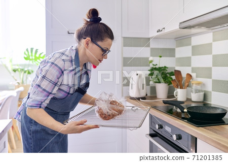 Woman preparing pork in baking sleeve at home, puts tray of meat in oven Woman preparing pork in baking sleeve at home, puts tray of meat in oven 71201385