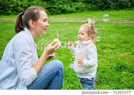 A Caucasian kid with his mother runs in the park in the summer for soap bubbles 71201577