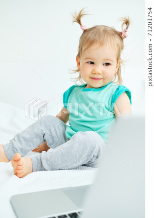 The child carefully looks into the laptop monitor while lying on the bed. Vertical. 71201754