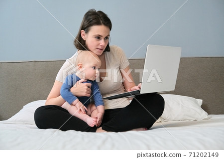 Young woman with son toddler sitting in bed with laptop computer 71202149