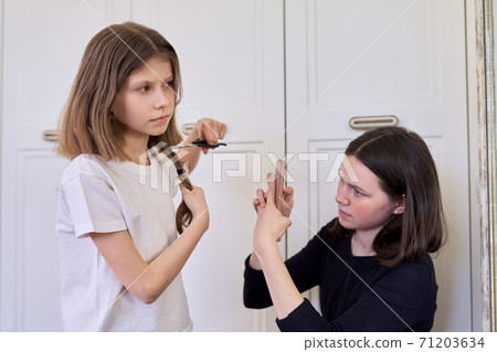 Girl child cuts her own hair with scissors, older sister teenager makes videos on smartphone Girl child cuts her own hair with scissors, older sister teenager makes videos on smartphone 71203634