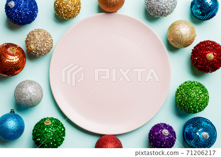 Top view of empty plate surrounded with colorful baubles on blue background. New Year decorations. Christmas Eve concept Top view of empty plate surrounded with colorful baubles on blue background. New Year decorations. Christmas Eve concept 71206217