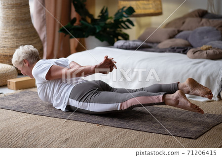 Senior woman practicing yoga at home indoor, doing Salabhasana or Locust pose. 71206415