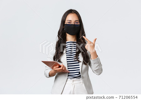 Business, finance and employment, covid-19 preventing virus and social distancing concept. Smiling asian businesswoman with digital tablet pointing at protective mask on face 71206554
