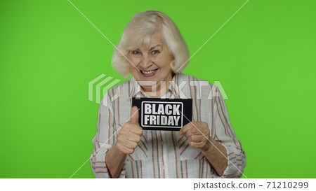 Senior grandmother showing Black Friday inscription note, smiling, looking satisfied with low prices 71210299