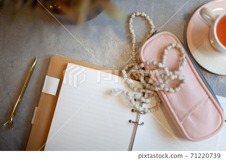 Opened notebook with clean sheets, gold pen, rosary, pink colored case and cup of tea near vase Opened notebook with clean sheets, gold pen, rosary, pink colored case and cup of tea near vase 71220739