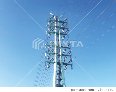 A view of a high-voltage tower in the center of the clear blue sky and a power transmission line 71222449
