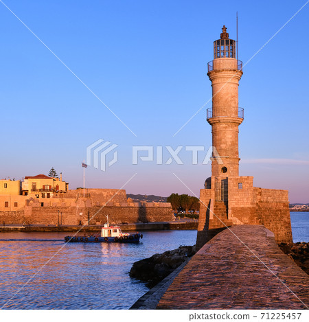Fishing boat pass by Lighthouse lit by first sunrays in Old Venetian harbour, Chania, Crete, Greece at sunrise. Square ratio, soft early morning. Fishing boat pass by Lighthouse lit by first sunrays in Old Venetian harbour, Chania, Crete, Greece at sunrise. Square ratio, soft early morning. 71225457
