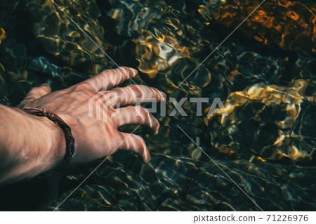 Close-up of a hand touching the surface of the water with light reflections Close-up of a hand touching the surface of the water with light reflections 71226976