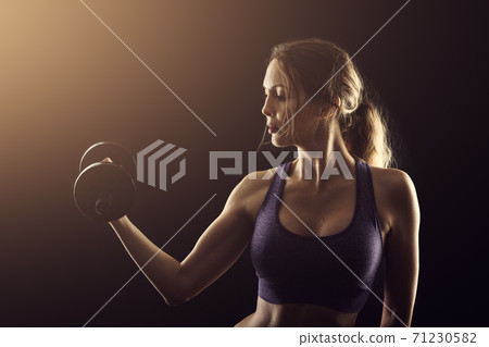 Slim athletic woman Holding dumbbell in the hand on black Slim athletic woman Holding dumbbell in the hand on black 71230582