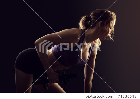 Slim athletic woman Holding dumbbell in the hand on black Slim athletic woman Holding dumbbell in the hand on black 71230585