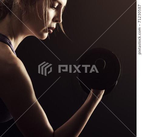 Slim athletic woman Holding dumbbell in the hand on black Slim athletic woman Holding dumbbell in the hand on black 71230587