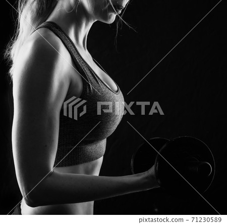 Slim athletic woman Holding dumbbell in the hand on black 71230589
