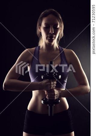 Slim athletic woman Holding dumbbell in the hand on black Slim athletic woman Holding dumbbell in the hand on black 71230595